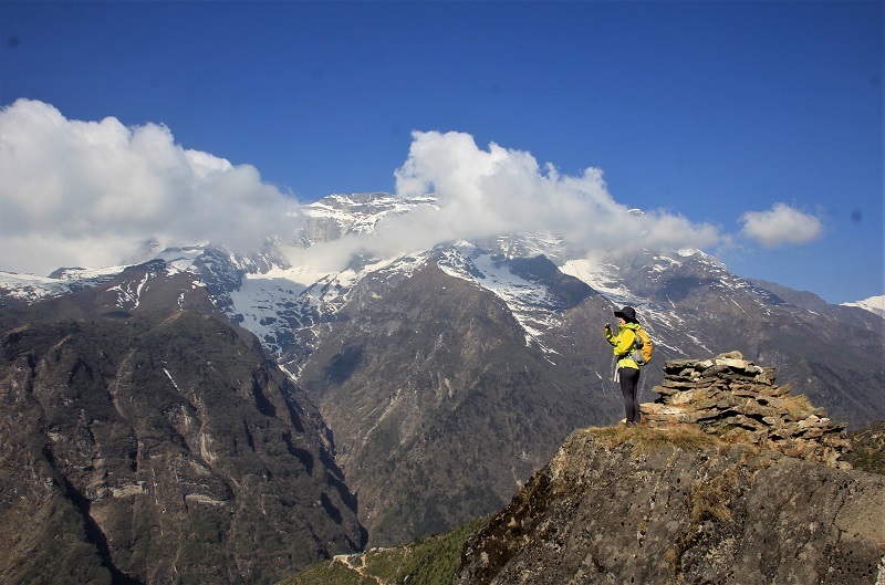 White snow covered mountains with clouds in between and a trekker standing in front