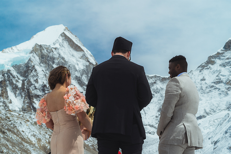 man in black coat in the middle of a man and a woman turned towards the mountain