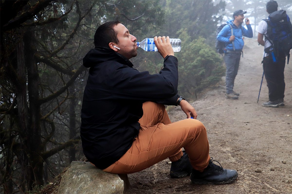 ​​Trekker drinking water from a water bottle and his two friends waiting for him on a hike